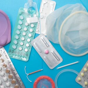 Assorted medical supplies scattered on a blue background: blister packs of pills, a pink silicone cup, tubing, and a plastic bag.